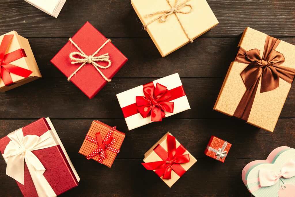 Assorted DIY-style gift boxes wrapped with red, brown, and white ribbons on a rustic wooden background.