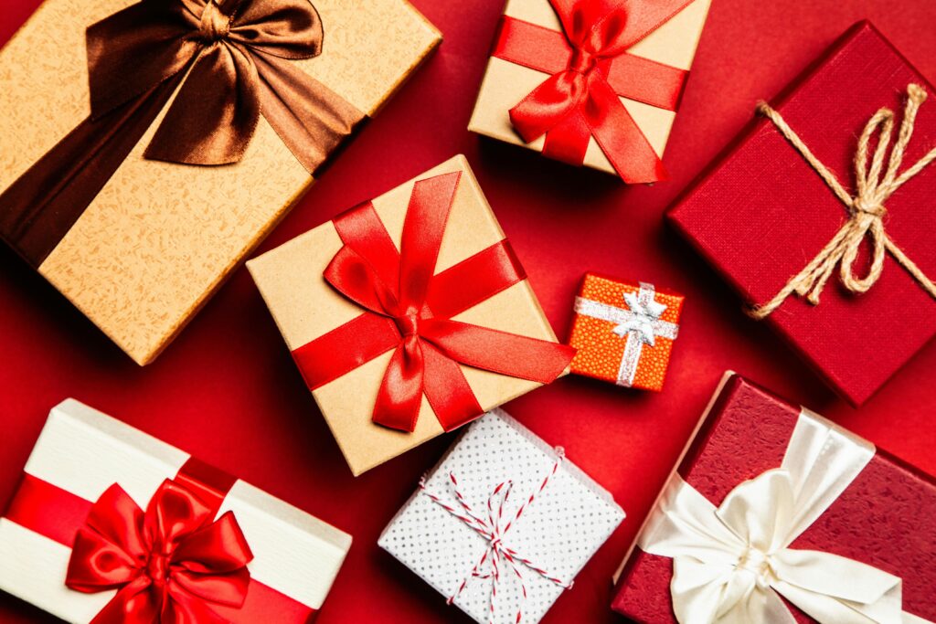 Assorted Christmas gifts wrapped in red, gold, and white paper with festive ribbons and bows on a red background.