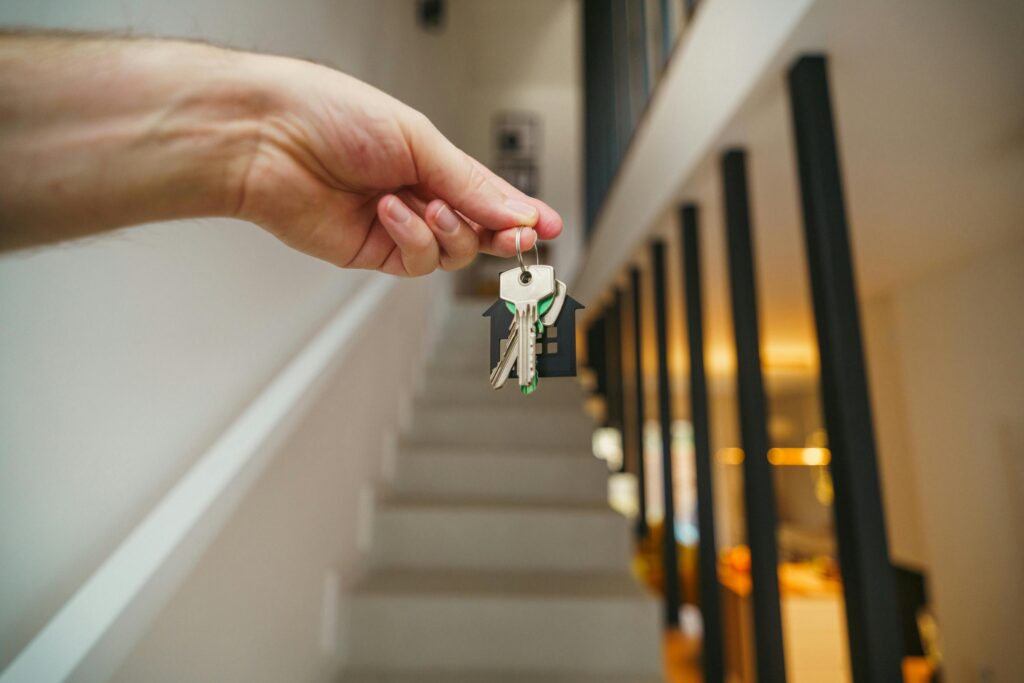 Hand holding a set of house keys inside a modern apartment, symbolizing new renters or tenants.