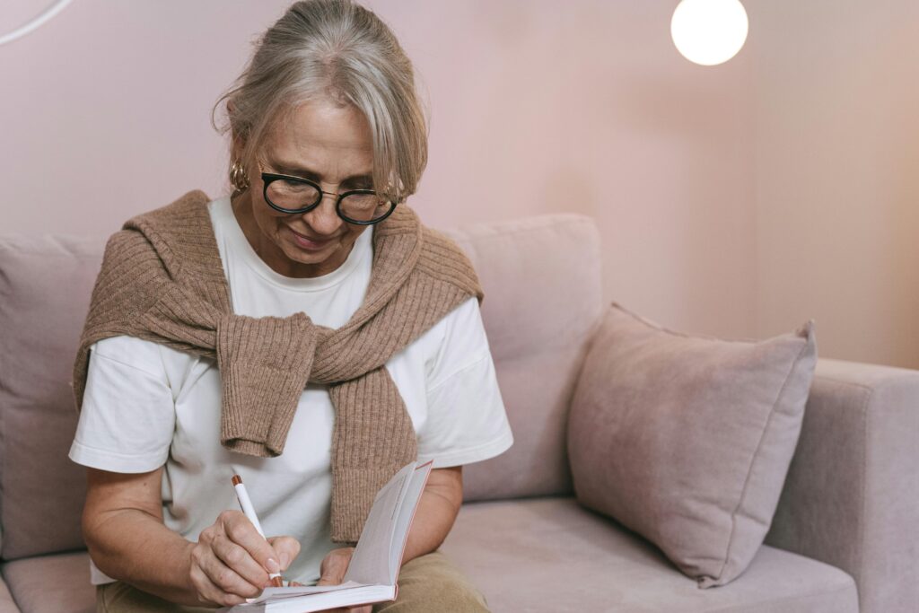 Older woman sitting on a couch writing notes in a notebook, symbolizing gaining college credit through life experience.