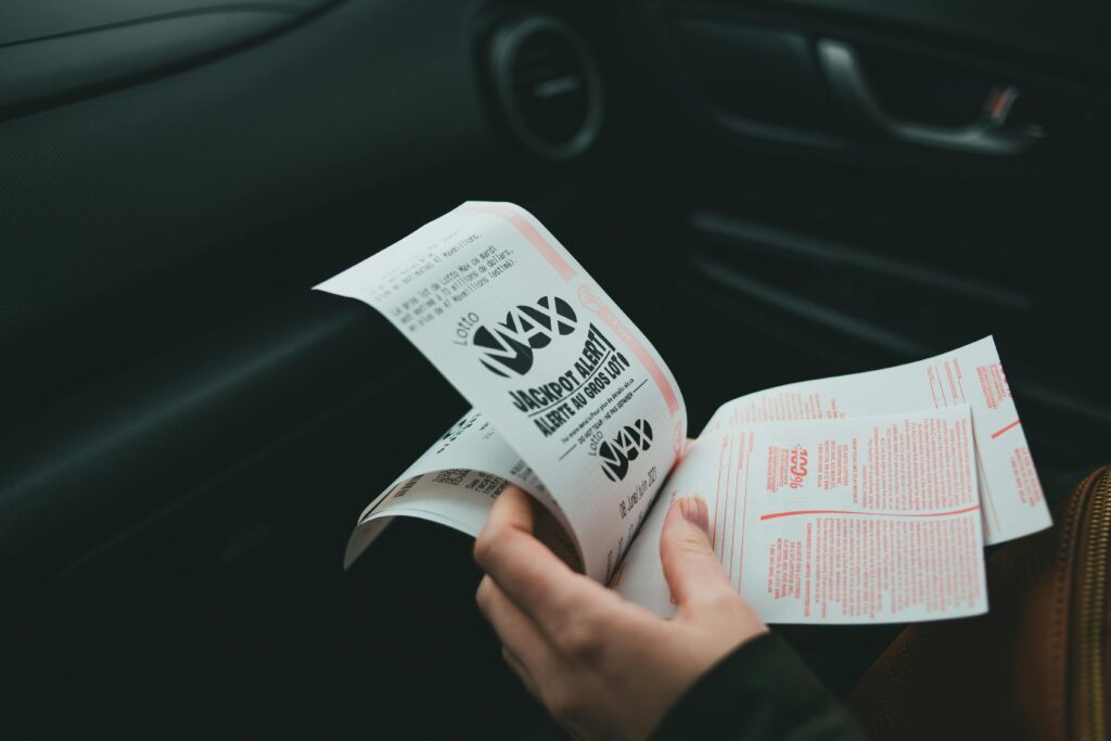 Close-up of a person holding a Lotto Max ticket inside a car, symbolizing the dream of winning big contrasted with the risks of relying on luck for financial security.