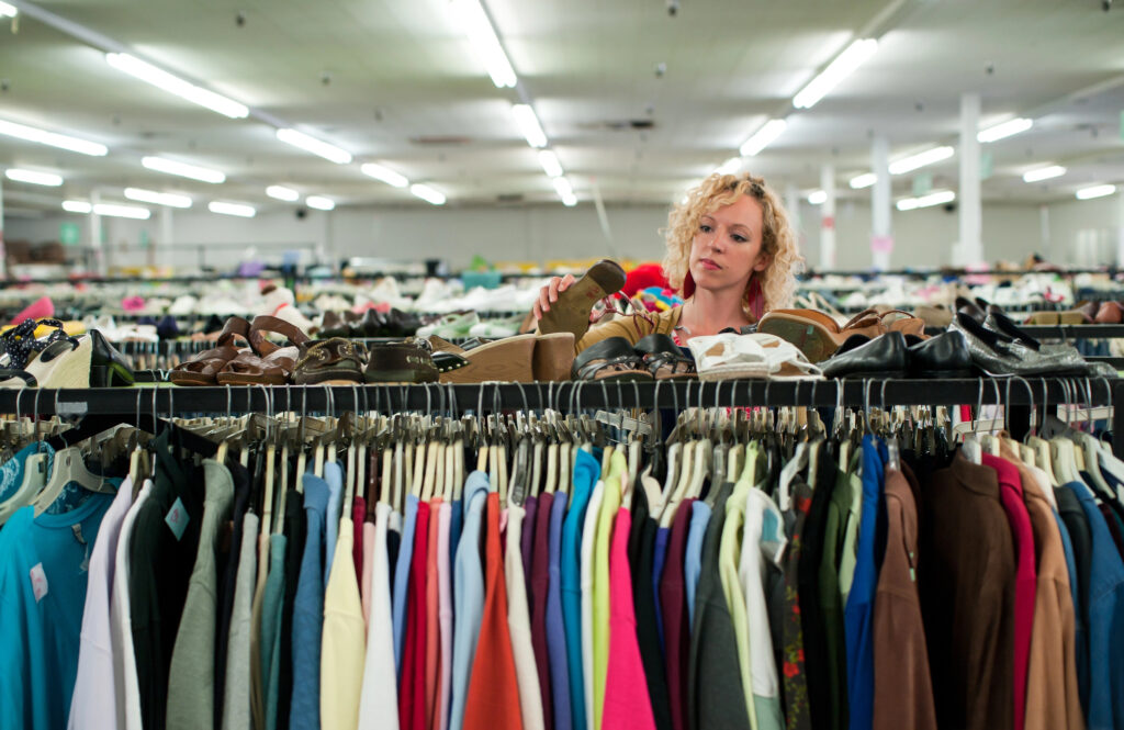 Woman browsing racks of clothes and shoes in a thrift store.