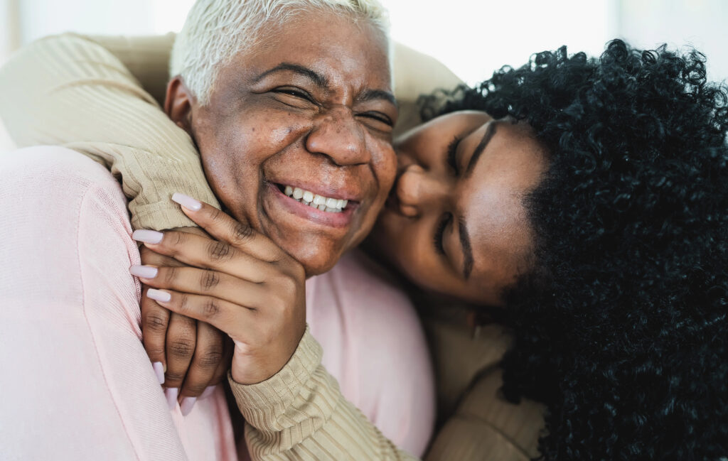 Daughter hugging and kissing her smiling mother, showing love and family support.