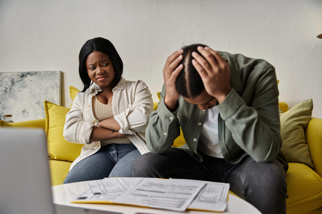 Couple sitting on a couch looking stressed while reviewing bills and financial paperwork.