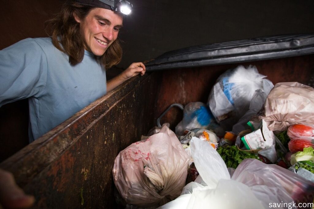 Person looking into a dumpster filled with discarded food while practicing Freeganism to reduce waste.