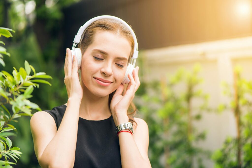 Woman relaxing outdoors while listening to a personal finance podcast through white headphones.