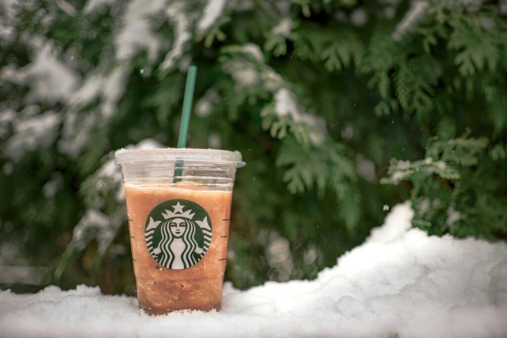 Iced Starbucks coffee sitting in the snow with green trees in the background.