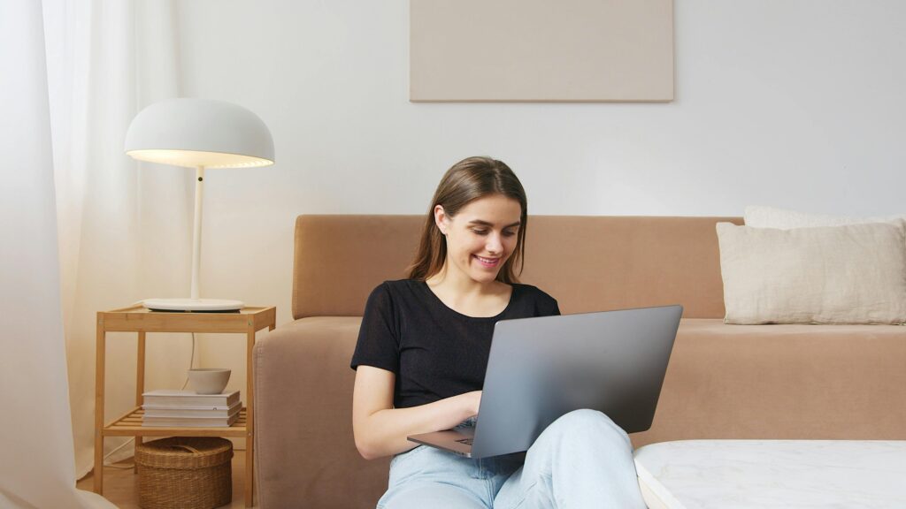 Woman sitting on the floor working on a laptop, creating digital products from home.