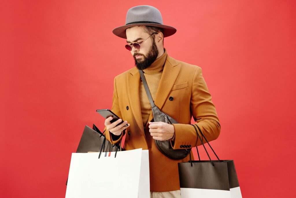 Stylish man shopping on Black Friday while checking deals on his phone against a red background.
