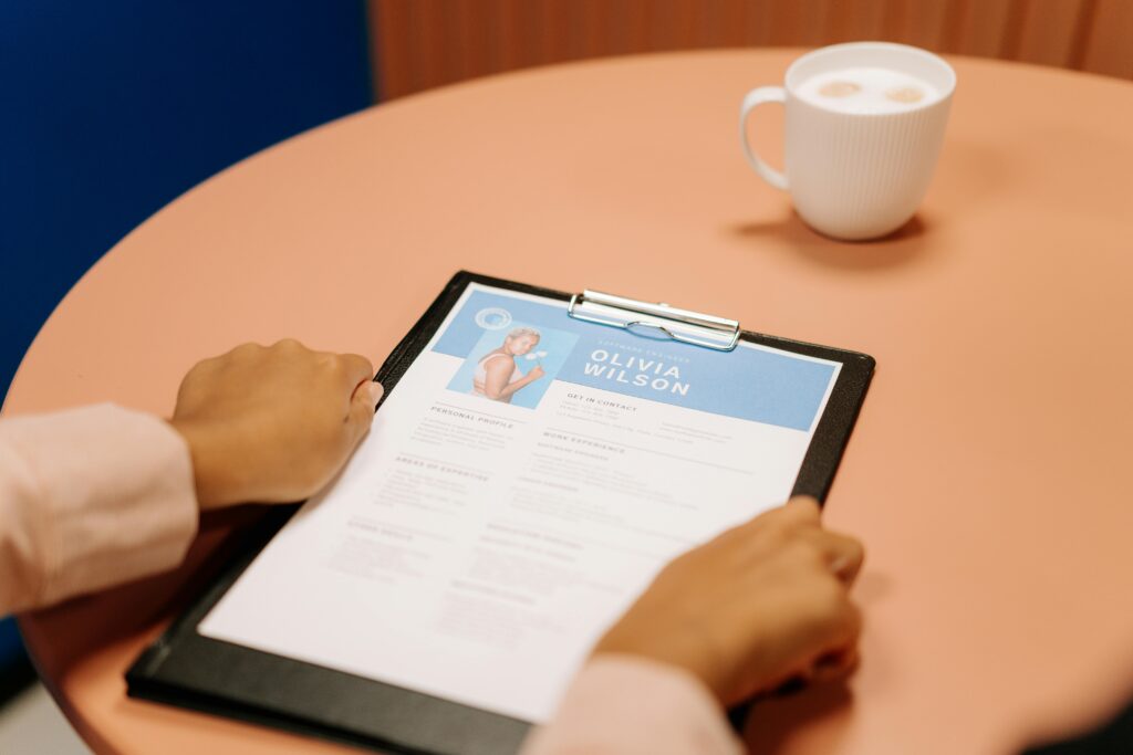 Person reviewing a professional resume on a clipboard at a desk with a cup of coffee.