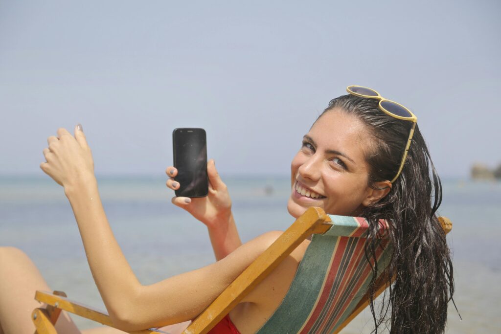 Woman relaxing in a beach chair holding a smartphone while enjoying a sunny vacation
