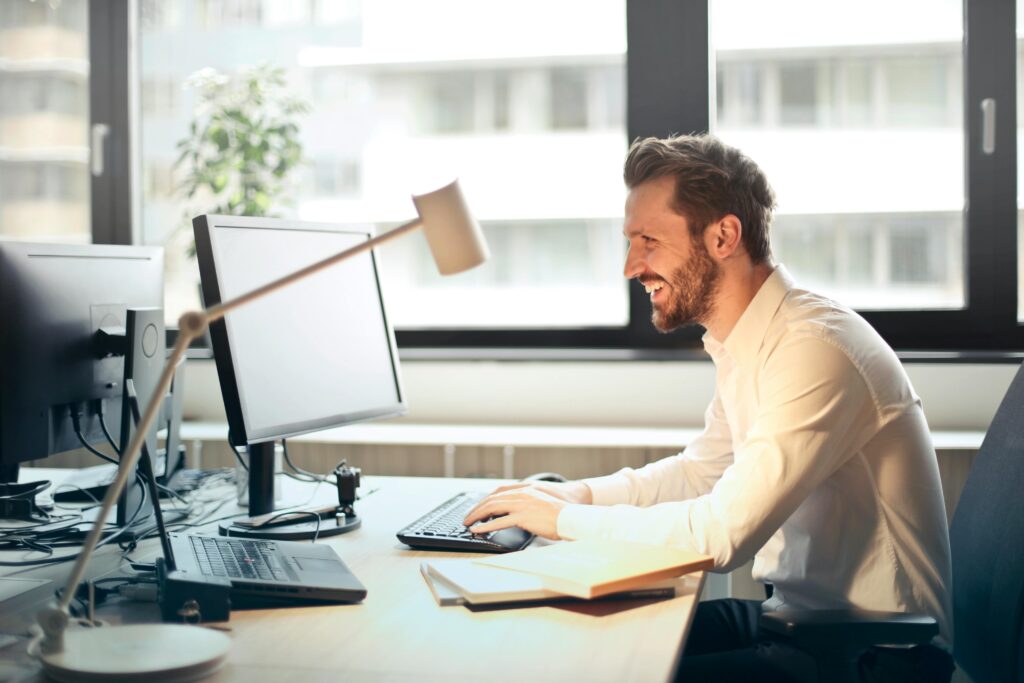 Man smiling while working on a computer in a bright modern office, representing online passive income opportunities.