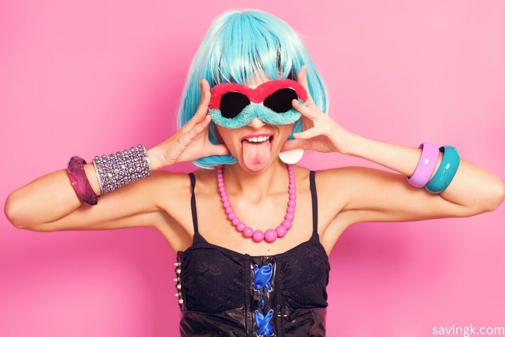 Woman with blue wig, colorful jewelry, and playful sunglasses making a funny face representing quirky and weird side hustle ideas.