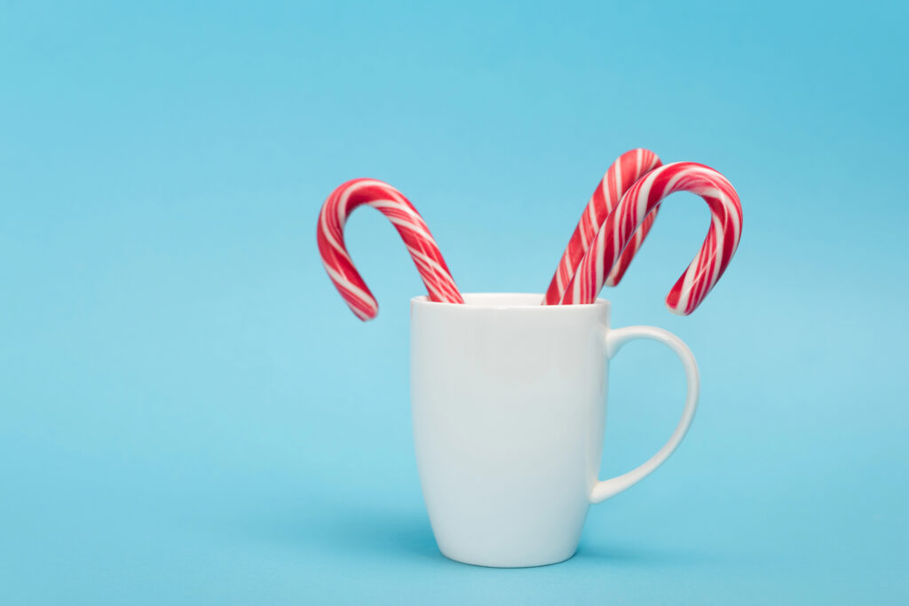 Two candy canes in a white mug on a blue background, showing a simple way to use leftover candy canes after Christmas.
