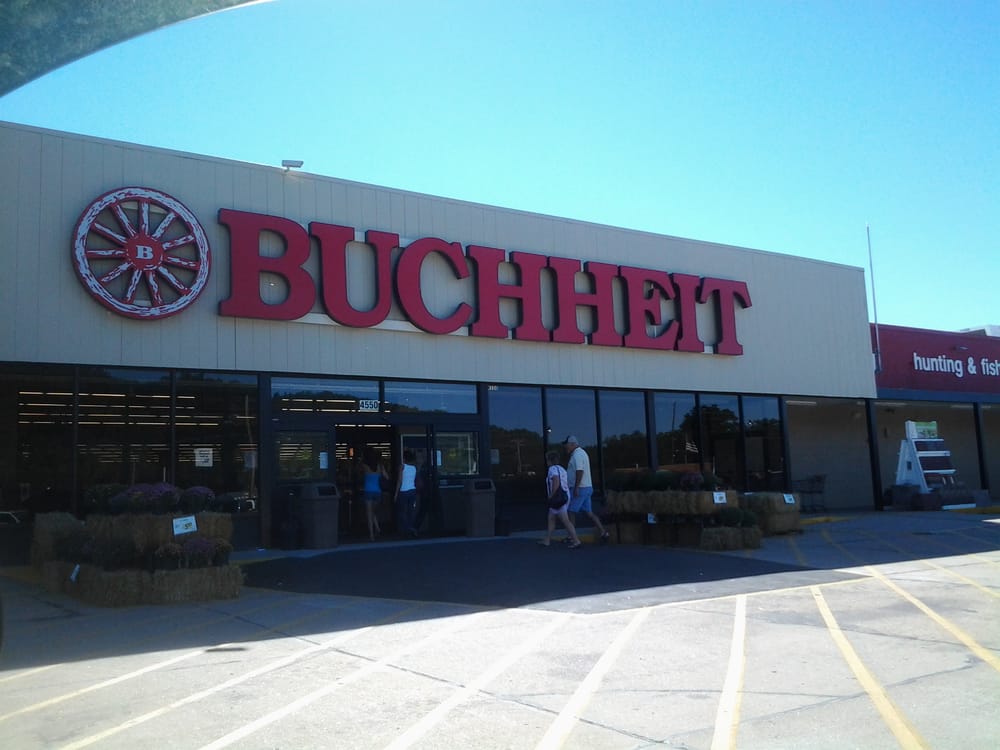 Exterior of a Buchheit store with large red lettering and shoppers entering the building on a sunny day.