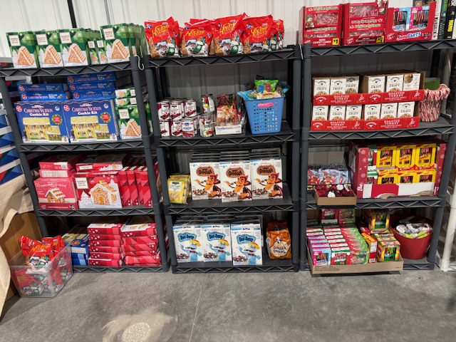 Shelving units filled with Christmas candy, gingerbread house kits, holiday snacks, and seasonal treats displayed in a store.