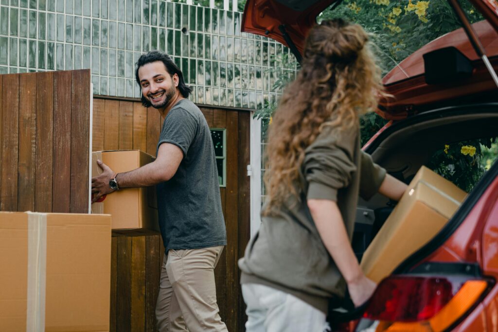 two people unloading cardboard boxes from a red car