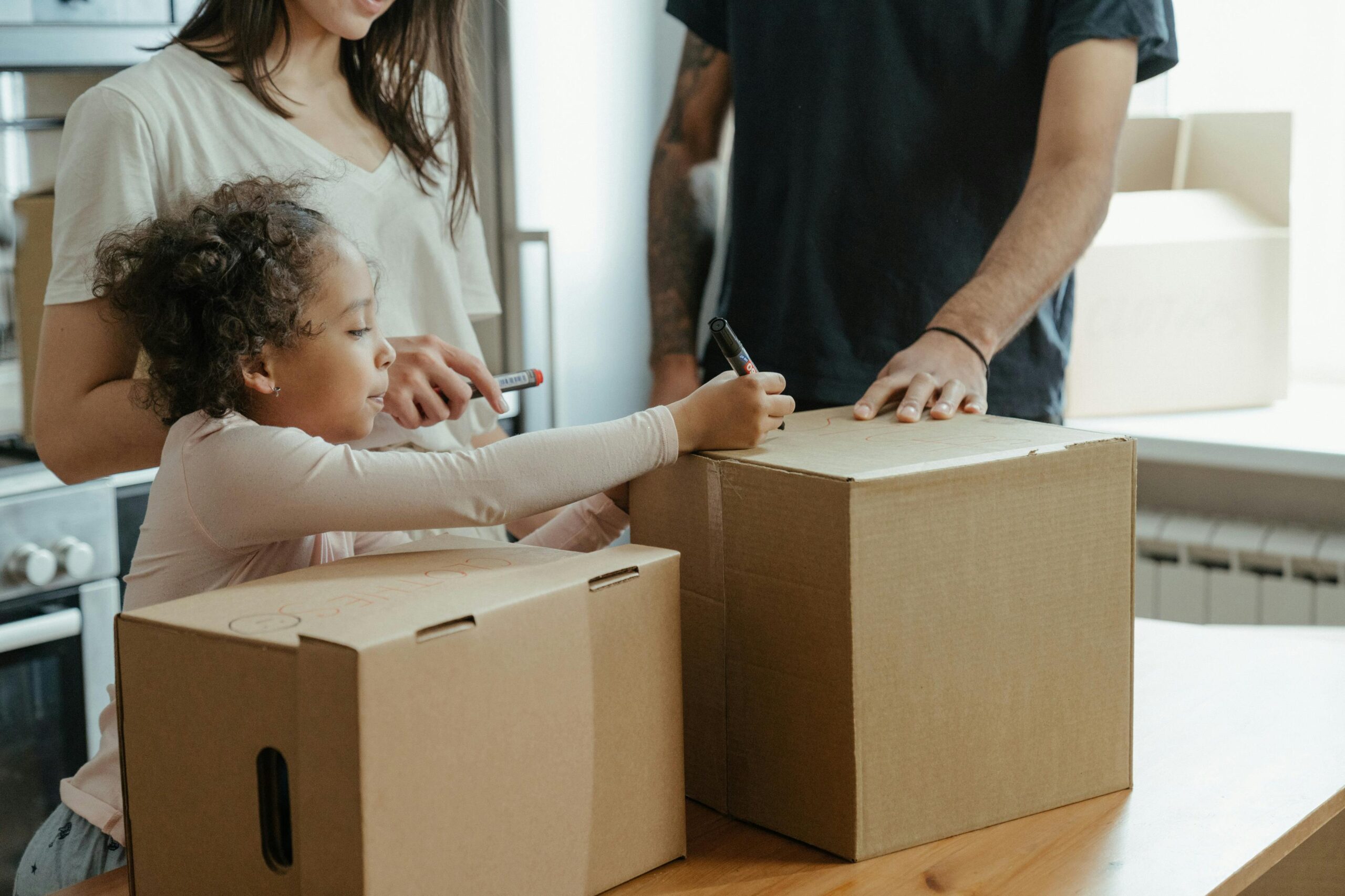 family packing or unpacking cardboard boxes in a kitchen setting, suggesting a move or organization activity