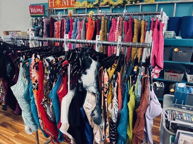 Colorful rack of women’s swimsuits organized by size inside a resale or liquidation boutique