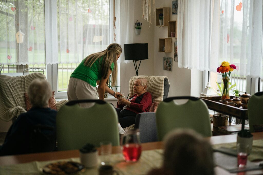 caregiver assisting elderly woman in assisted living room with natural light and comfortable setting