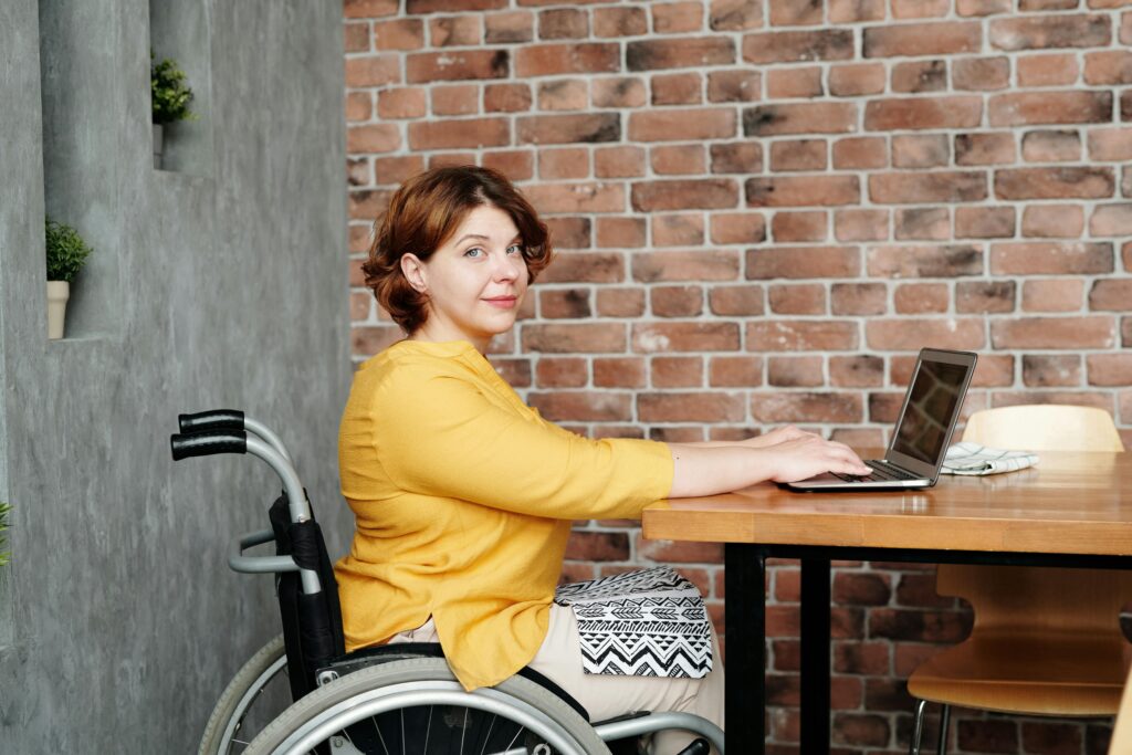 Woman in a wheelchair working on a laptop at a table, representing earning income while on disability benefits