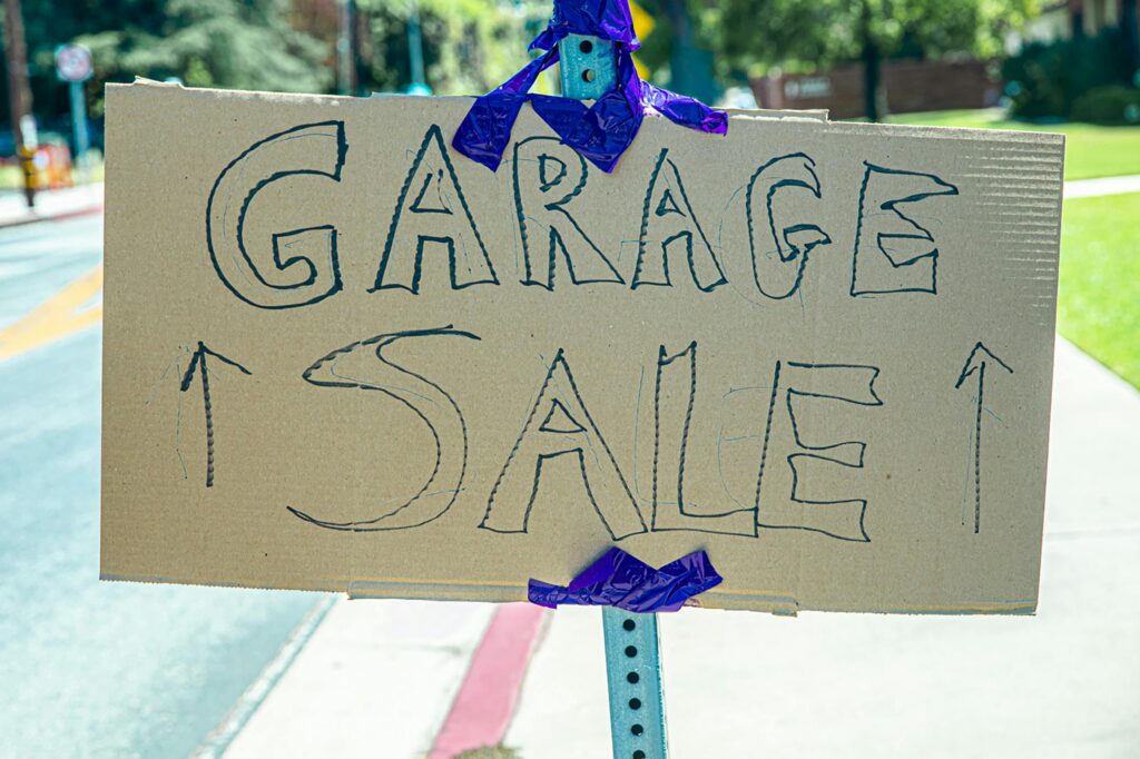 Handwritten garage sale sign on cardboard with arrows pointing directions