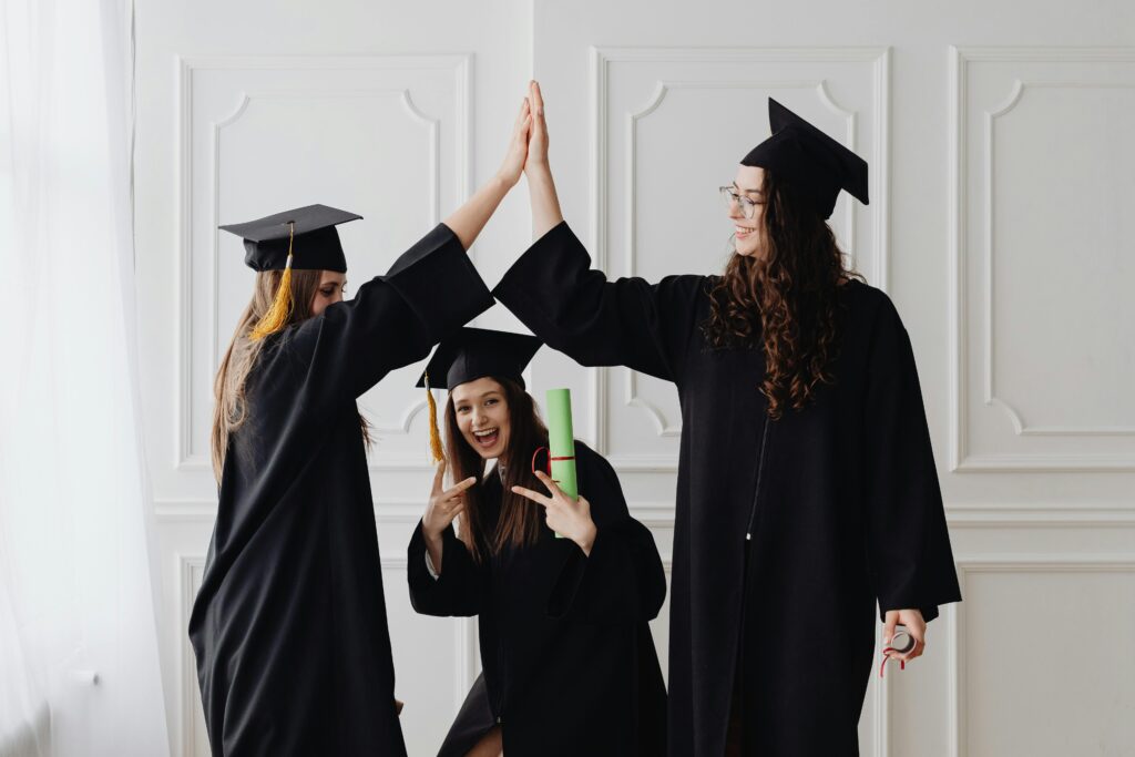 Three graduates in caps and gowns celebrating with a high five and holding diplomas