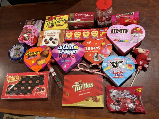 Assorted Valentine’s Day candy including chocolates, gummies, conversation hearts, Reese’s, M&M’s, Turtles, and candy canes displayed on a table