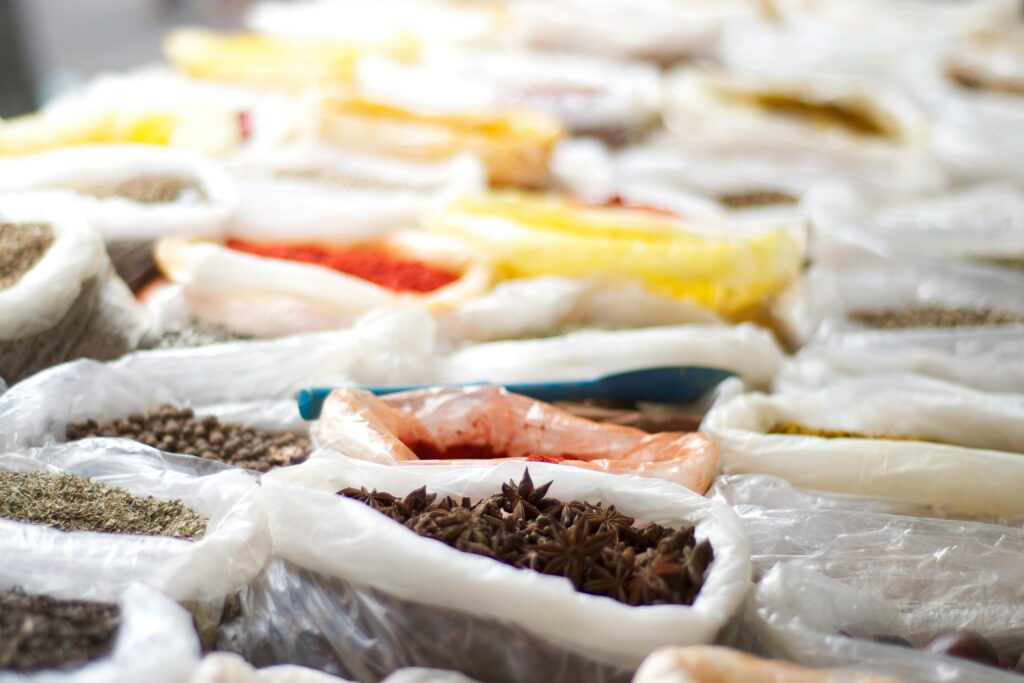 Open market display featuring bags of spices, herbs, seeds, and other bulk commodities arranged in rows.