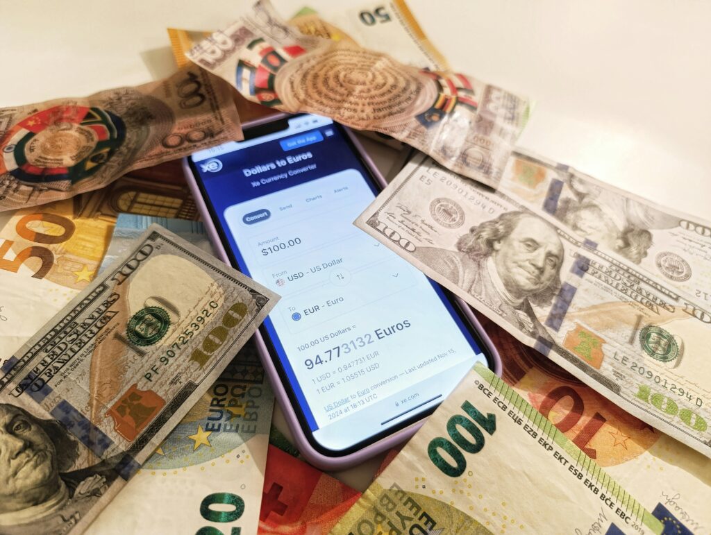 Smartphone displaying a currency conversion app surrounded by U.S. dollars and foreign banknotes representing international money transfers and exchange rates.