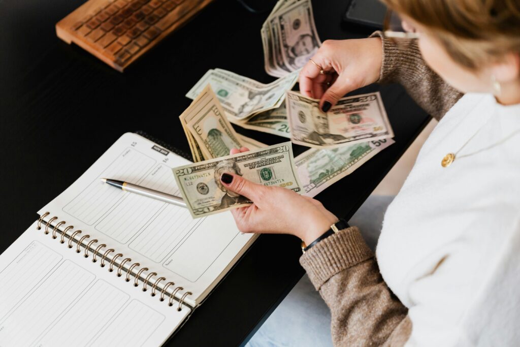 Woman counting cash while reviewing a budget planner at a desk