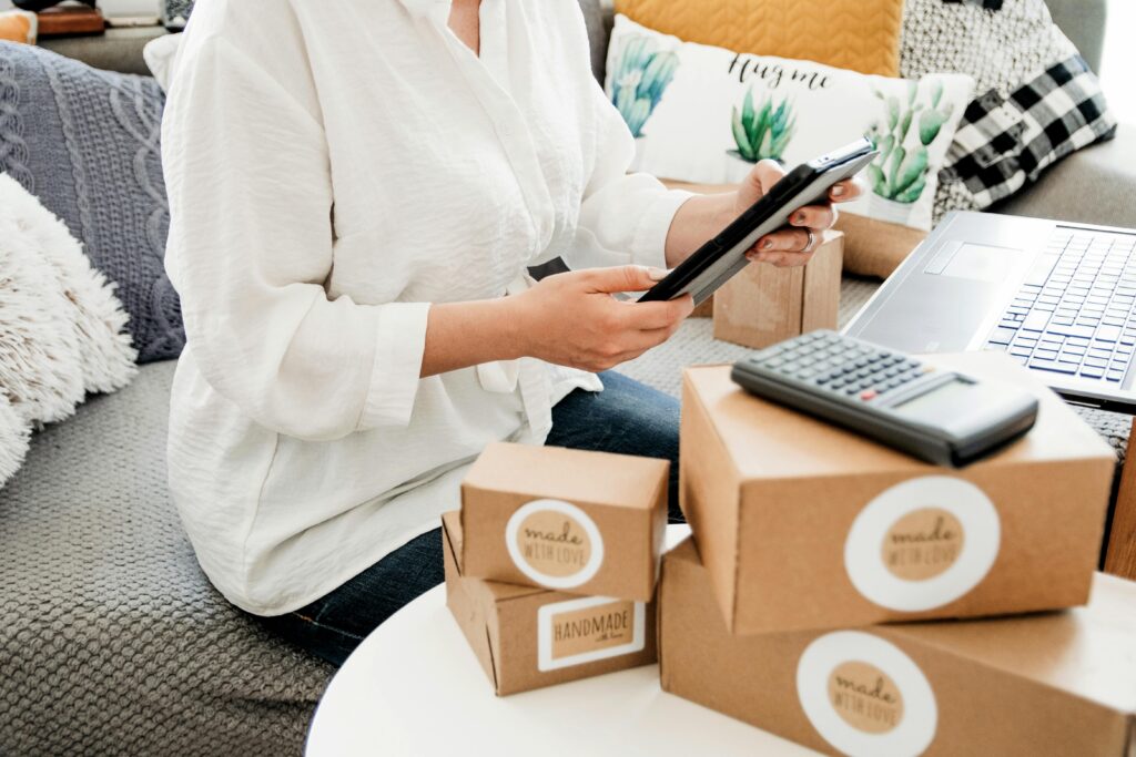 Person packaging online sales items while using a laptop and calculator at home