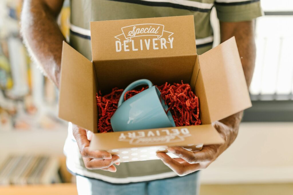 Person holding an open subscription box with packaging filler and a blue mug inside