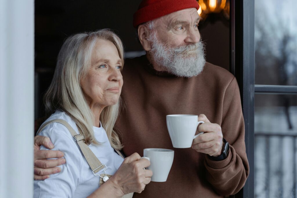 Older couple standing together by a window holding coffee mugs while planning for retirement and long-term financial security.