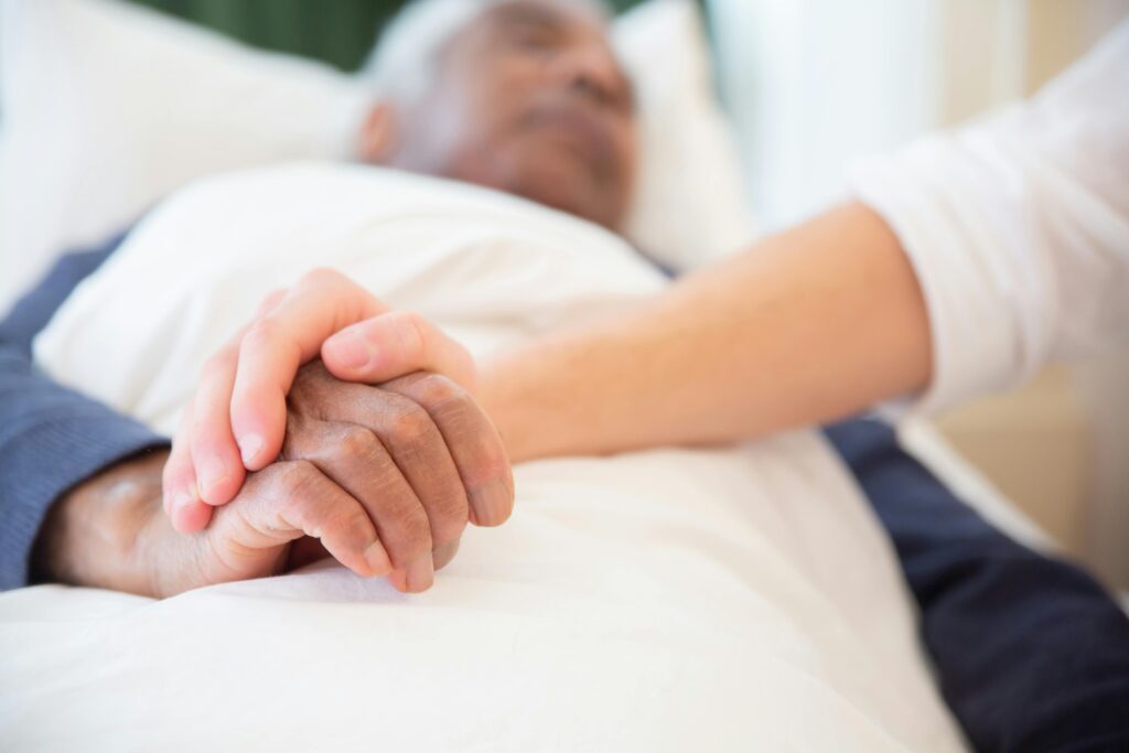 Caregiver holding the hand of an elderly hospice patient in bed