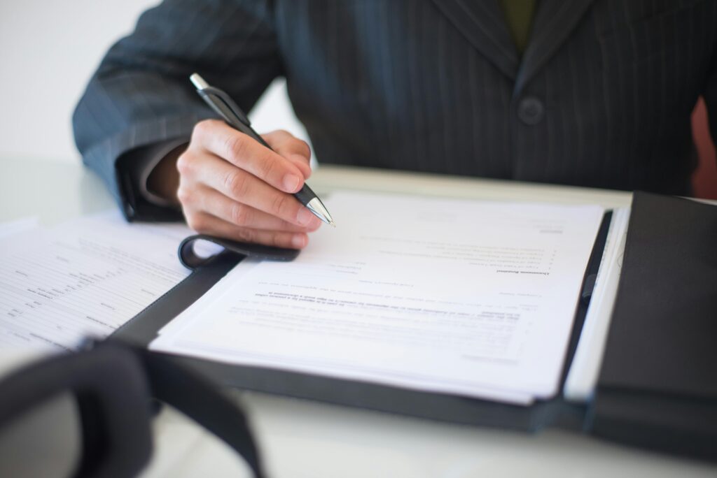 Person signing legal documents while reviewing an online will or estate planning paperwork