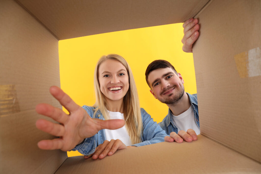 View from inside an empty cardboard shipping box as two smiling people prepare to pack and ship an order.