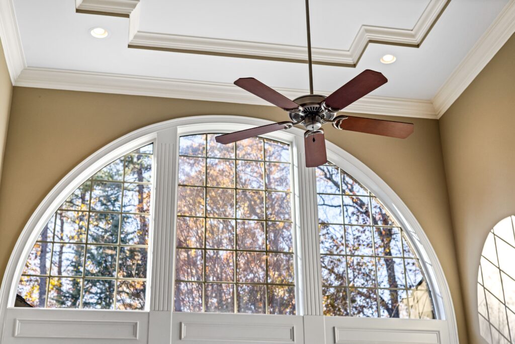 Ceiling fan spinning above large arched windows in a bright living room, demonstrating an energy-efficient way to stay comfortable while reducing heating and cooling costs.