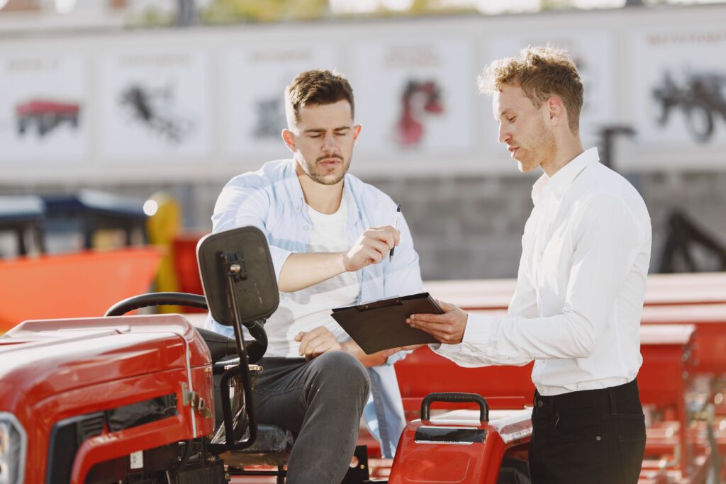 Customer reviewing paperwork with a sales representative while sitting on a red tractor at a dealership.
