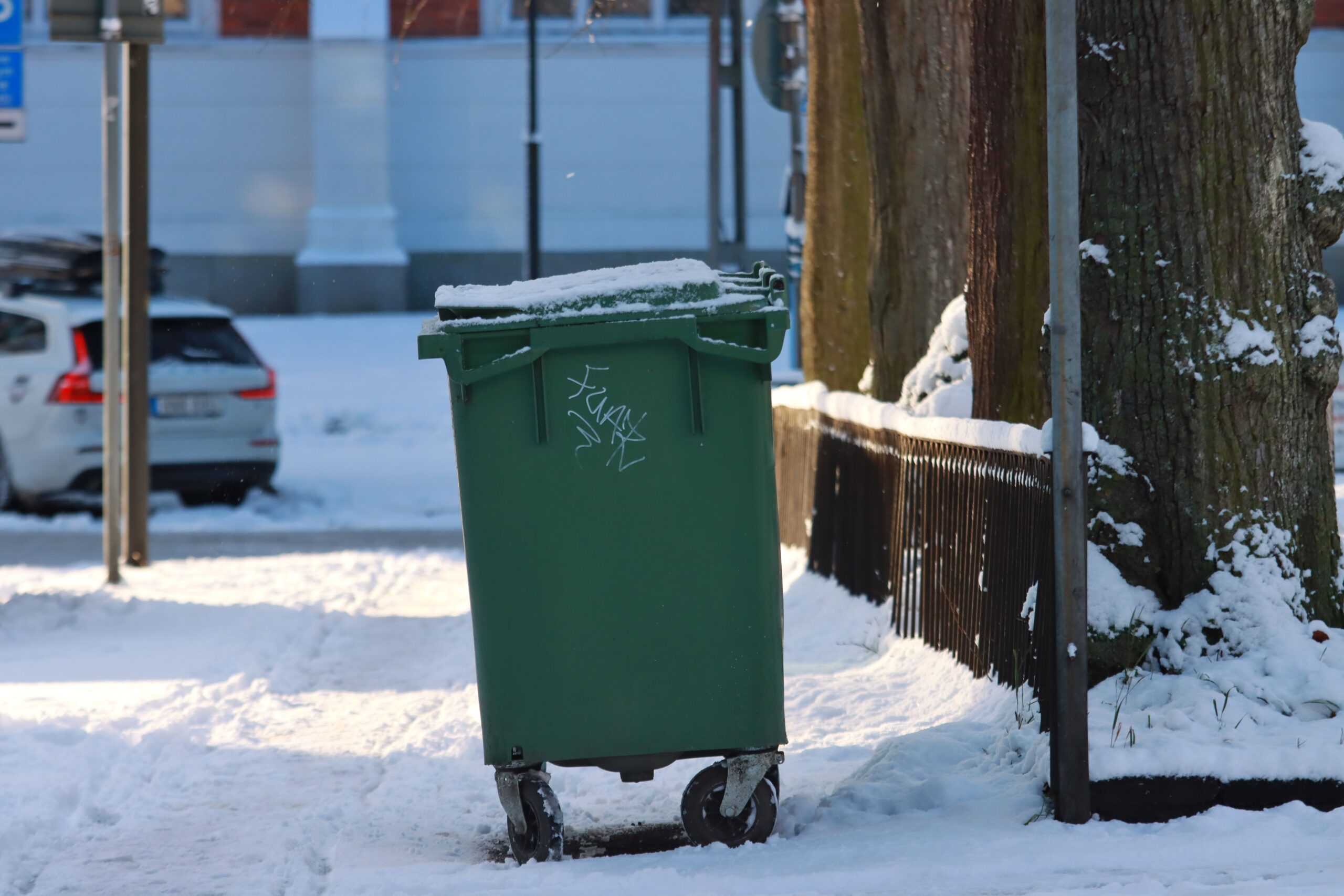 a green garbage bin on the street