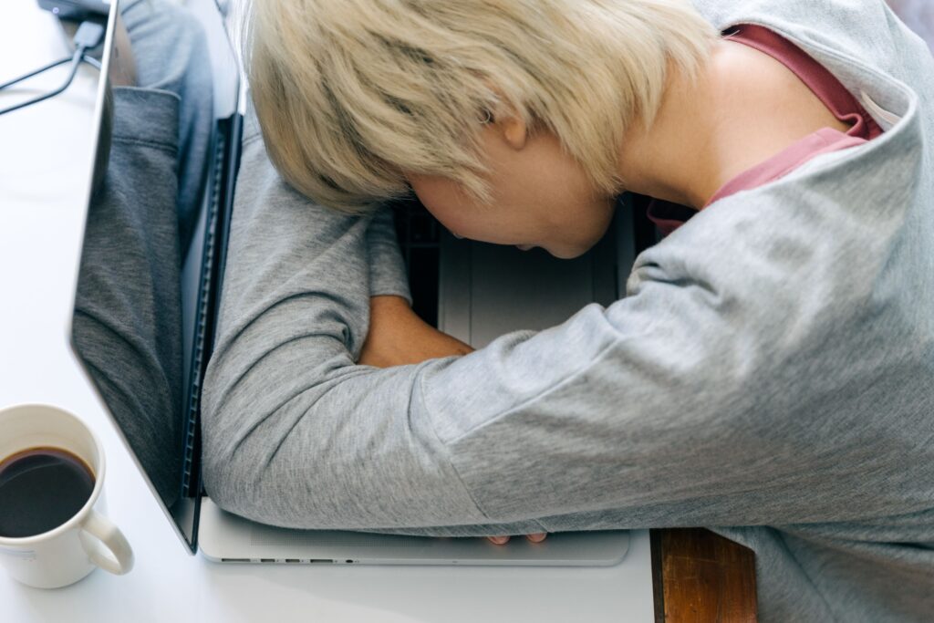 Person resting their head on a laptop keyboard at a desk, illustrating mental exhaustion and financial burnout.