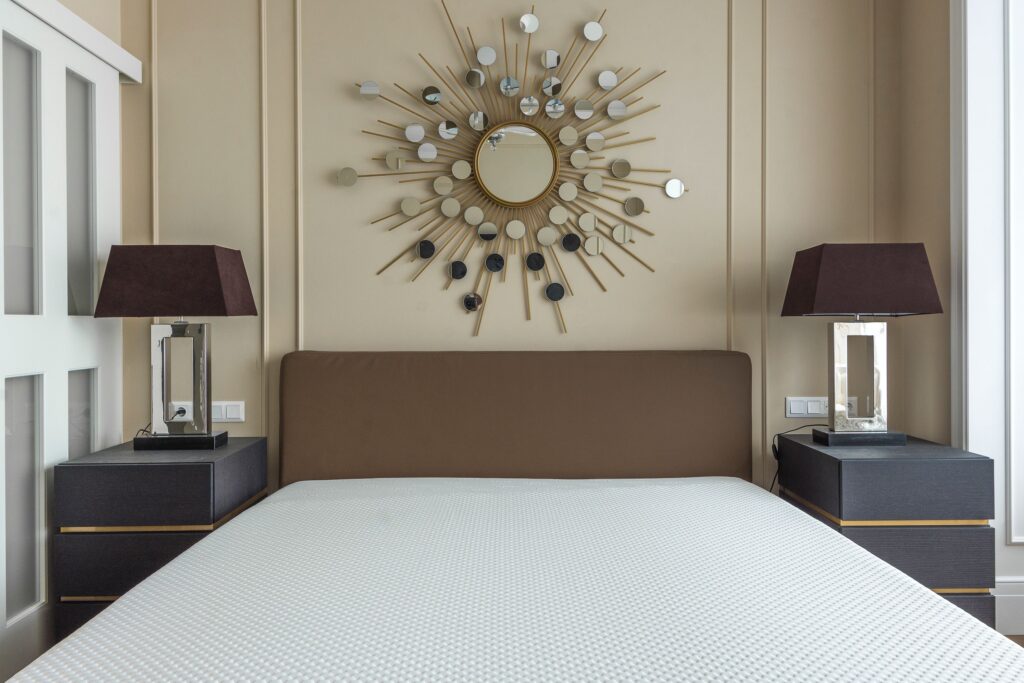 Modern bedroom featuring a white memory foam mattress on a platform bed with matching nightstands, table lamps, and a decorative sunburst mirror above the headboard.