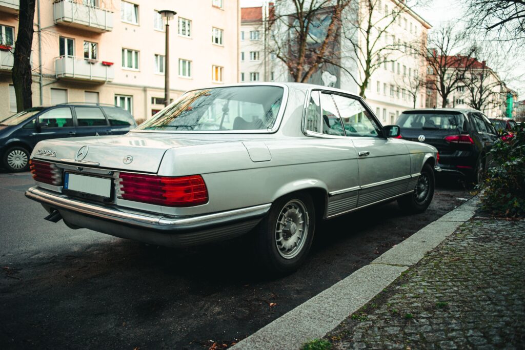 Vintage silver Mercedes-Benz 280 SLC parked on a city street, illustrating the costs to consider before buying a restored collector vehicle.