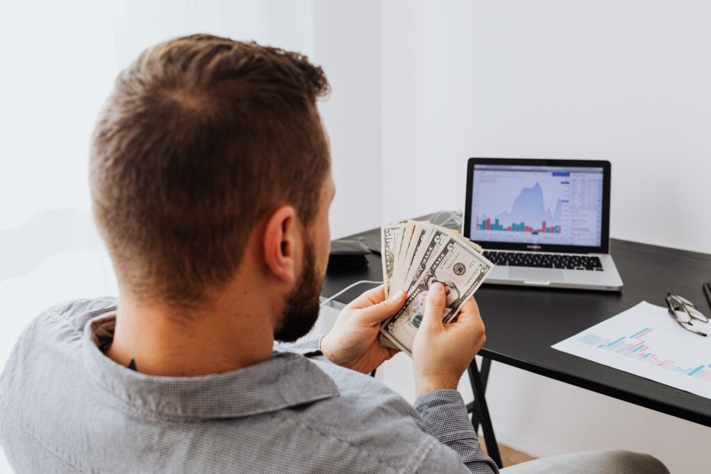 Man counting money while working on a laptop, representing earning commissions through sub-affiliate networks.