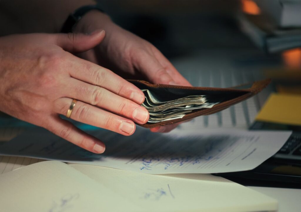 hands holding an open wallet filled with cash above documents