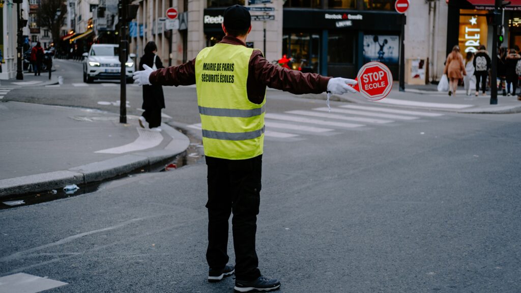 Traffic safety worker wearing a reflective yellow vest holding a stop sign while directing traffic at a city intersection.
