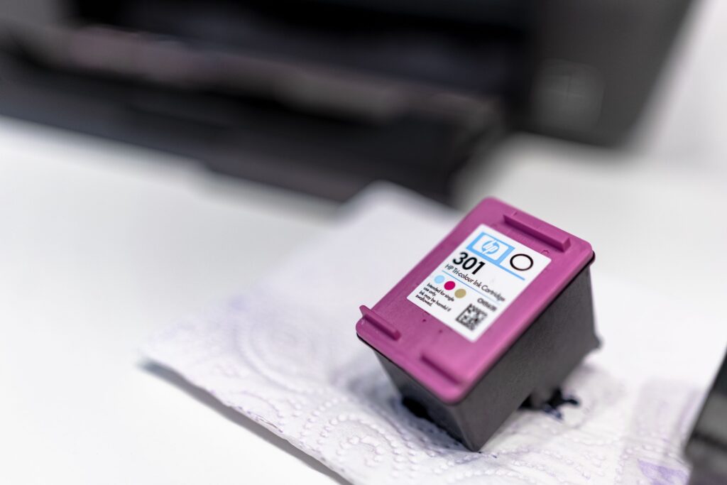 HP 301 tri-color printer ink cartridge resting on a paper towel near a printer.
