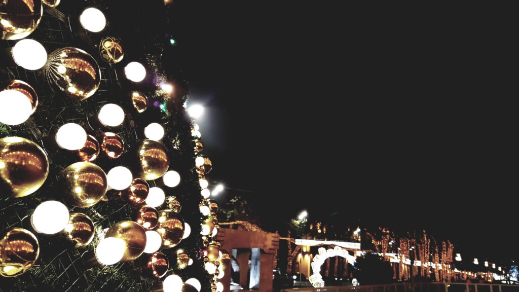 Beautiful Christmas tree decorated with glowing white lights and gold ornaments overlooking a festive holiday light display at night.