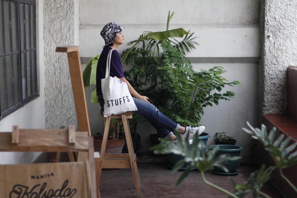 Woman sitting outdoors with a white canvas tote bag featuring the word STUFFS.